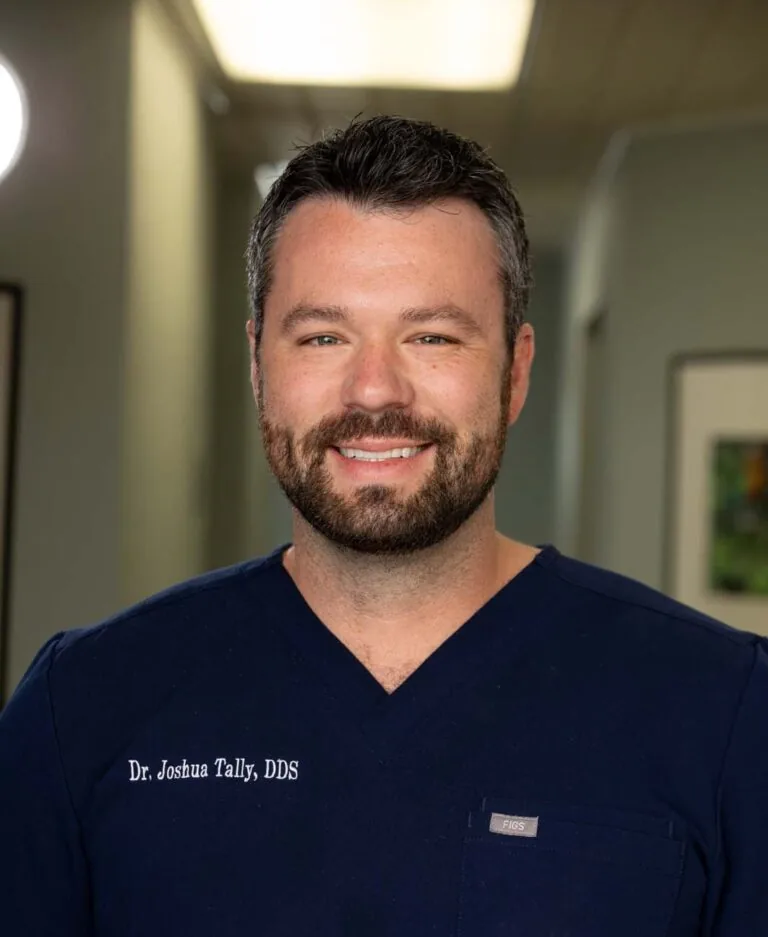 Headshot of Dr. Joshua wearing a dark blue scrub with his name on it. He is standing in a hallway.