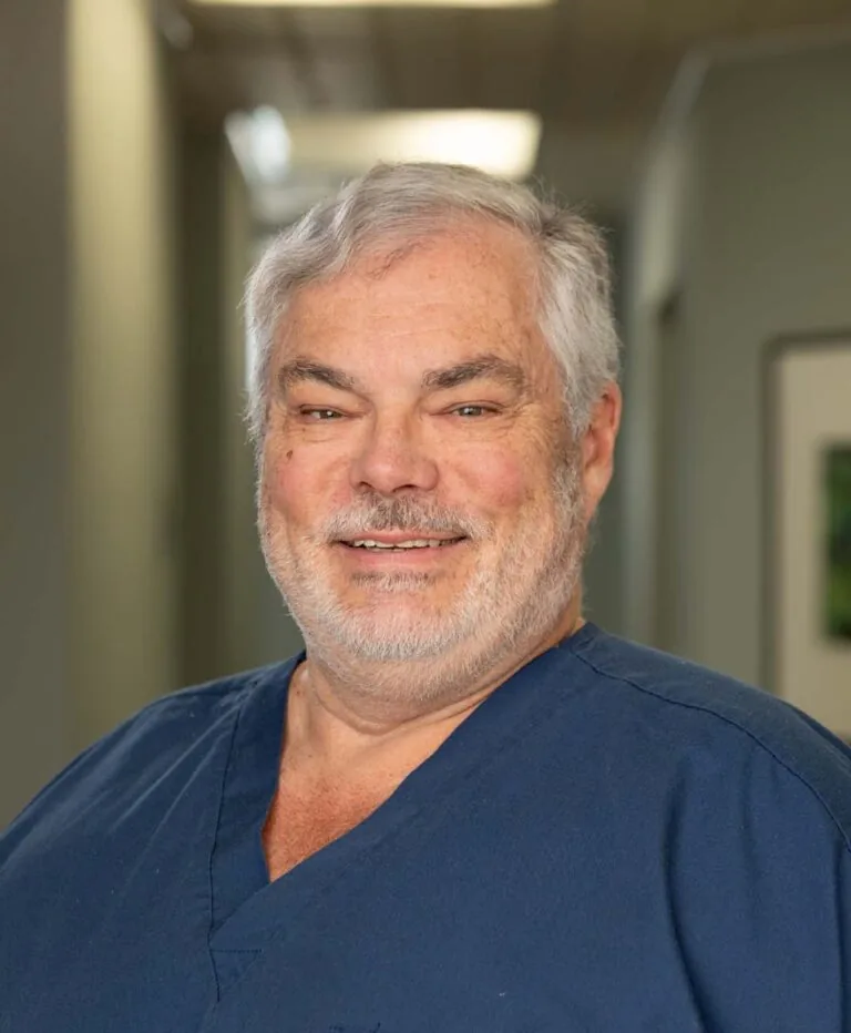 Headshot of Dr. Paul wearing a dark blue scrubs and standing against a hallway.