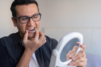 Close-up of a man placing a clear night guard on teeth with a mirror in hand, illustrating dental care at Tally Dental Excellence.